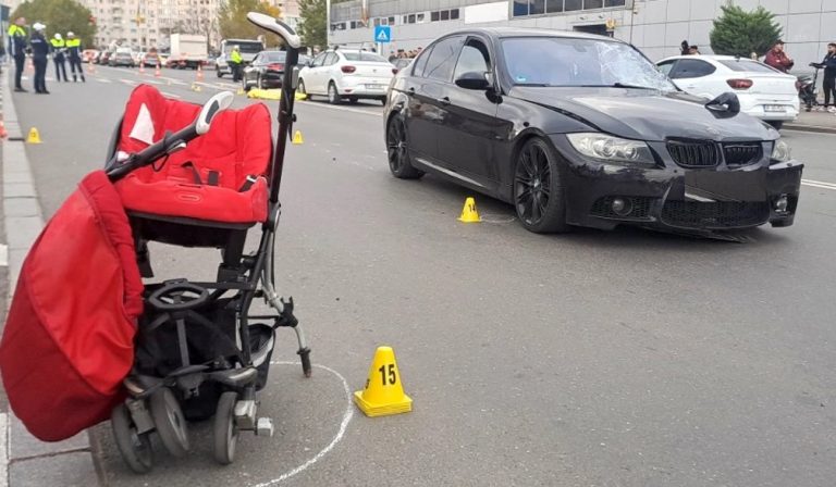 Accident rutier grav între un BMW negru și un cărucior roșu de copil pe o stradă urbană, investigat de poliție.