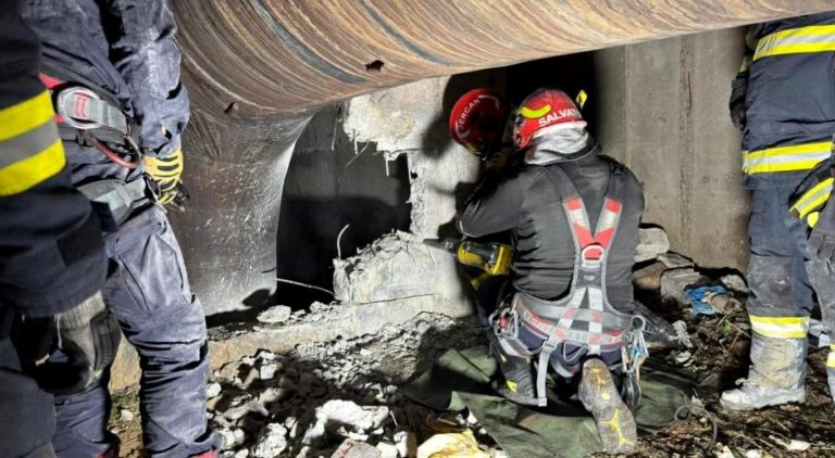 Pompieri salvatori intervenind într-un spațiu îngust sub o conductă mare, folosind echipamente de descarcerare pentru o operațiune de salvare