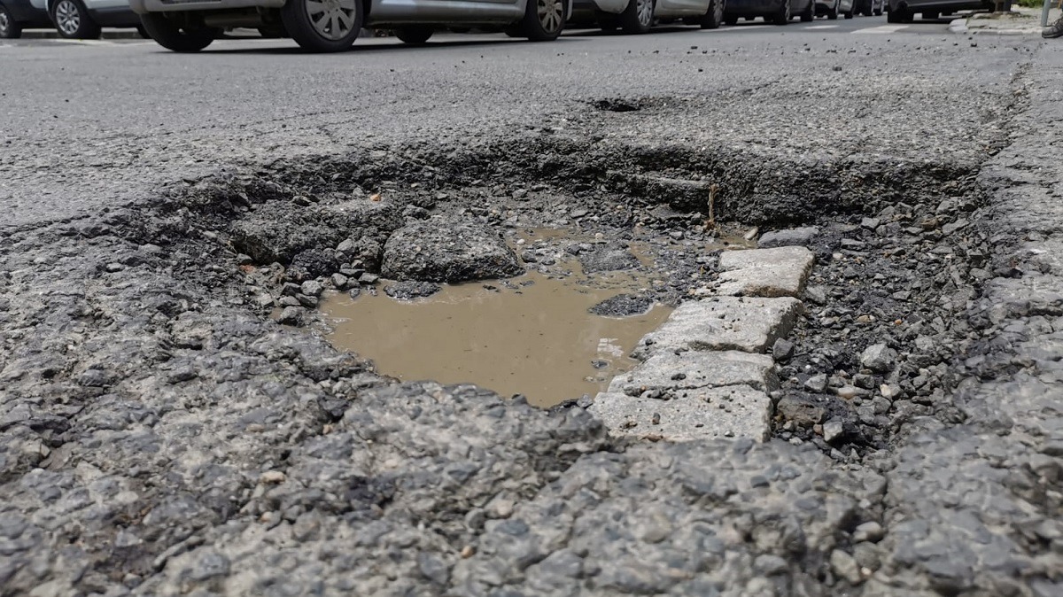 Groapă adâncă cu apă pe o stradă din București, evidențiind starea precară a infrastructurii rutiere și necesitatea reparațiilor urgente.