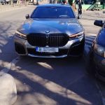 BMW gri parcat pe trotuar lângă o altă mașină, ocupând spațiul destinat pietonilor într-o zonă urbană.
