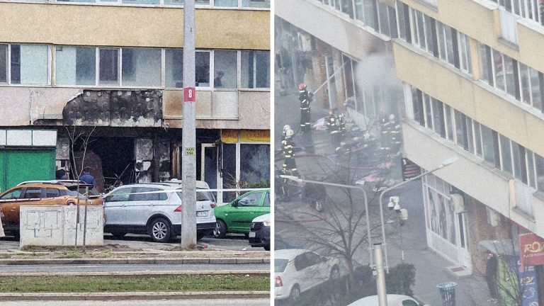 Pompieri intervenind pentru stingerea unui incendiu la parterul unui bloc de locuințe, fațadă de magazin distrusă de flăcări și fum.