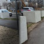 Blocuri de beton amplasate pe marginea trotuarului lângă o stradă urbană cu mașini și lucrări rutiere