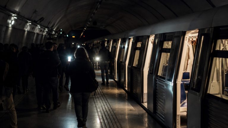 Pasageri evacuând un tren de metrou în timpul unei pene de curent, într-un tunel slab iluminat.