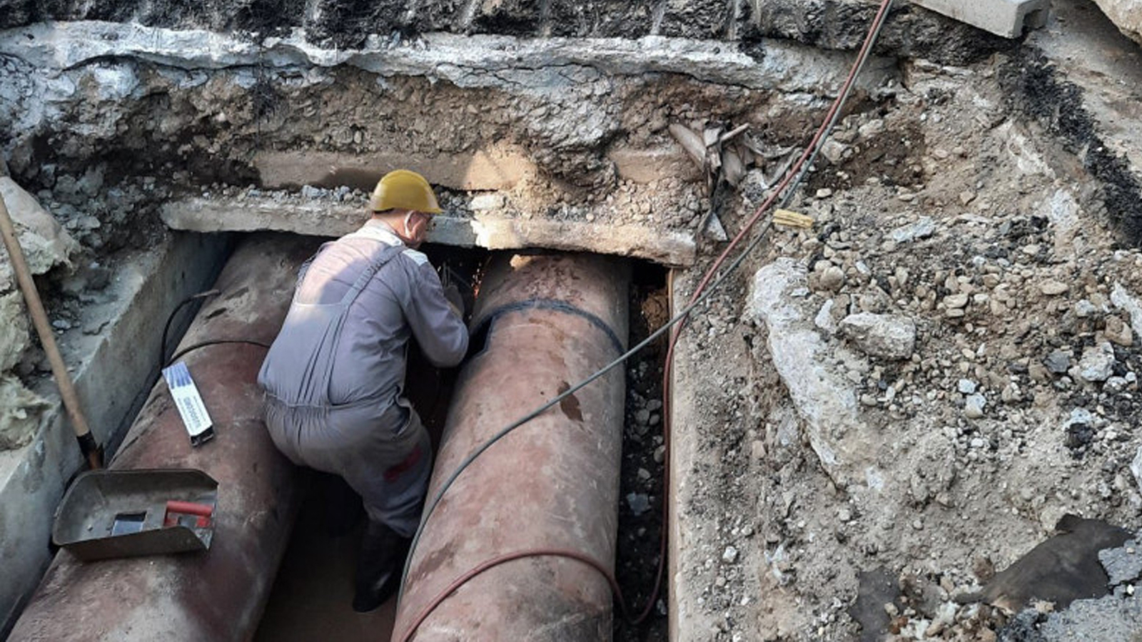 Lucrător la rețeaua de termoficare executând lucrări de reparație la conducte subterane de apă caldă într-o zonă excavată, pentru remedierea unei avarii termoenergetice.