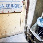 Ușă de acces către ghena de gunoi a unui bloc de locuințe, cu inscripția „Ușa se încuie”, într-o zonă tehnică destinată colectării deșeurilor menajere.