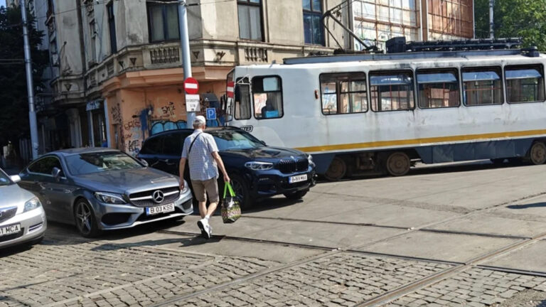 BMW parcat pe linia de tramvai, într-o zonă urbană aglomerată, lângă alte autoturisme și un tramvai.