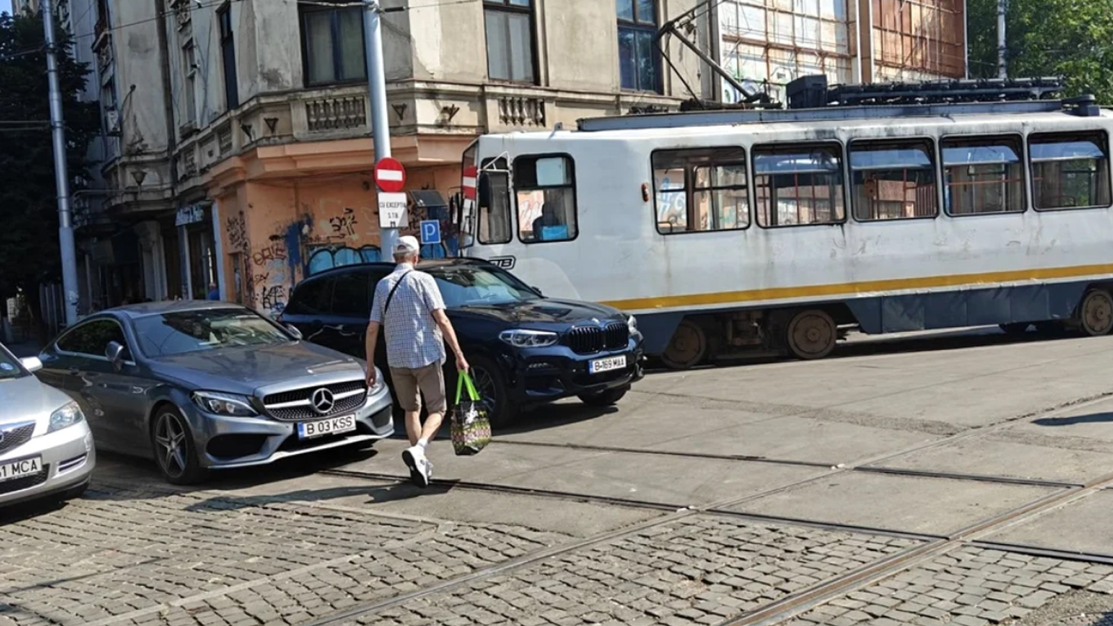 BMW parcat pe linia de tramvai, într-o zonă urbană aglomerată, lângă alte autoturisme și un tramvai.