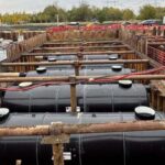 Rezervoare mari de stocare subterană din plastic negru montate într-o excavație securizată pe un șantier de construcții industriale.