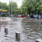 Autobuz STB circulând printr-o stradă inundată din București, cu mașini blocate parțial în apă după ploi abundente.