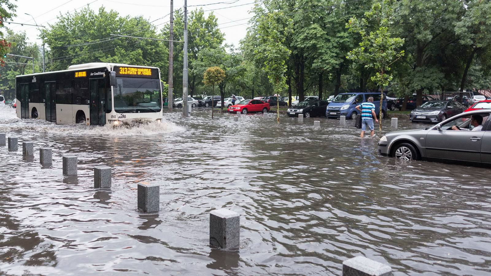 Autobuz STB circulând printr-o stradă inundată din București, cu mașini blocate parțial în apă după ploi abundente.