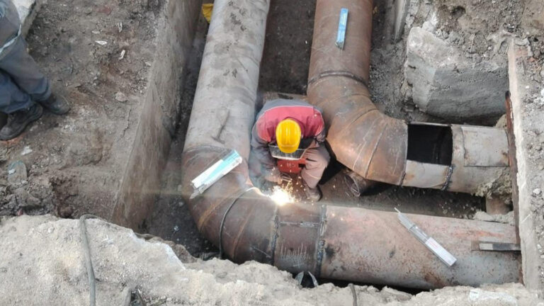 Muncitor care execută lucrări la rețeaua de termoficare, sudând conducte metalice într-un șantier subteran.