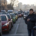 Cetățean îngrijorat uitându-se la ceas în mijlocul unui ambuteiaj urban, sugerând timpul pierdut în trafic.
