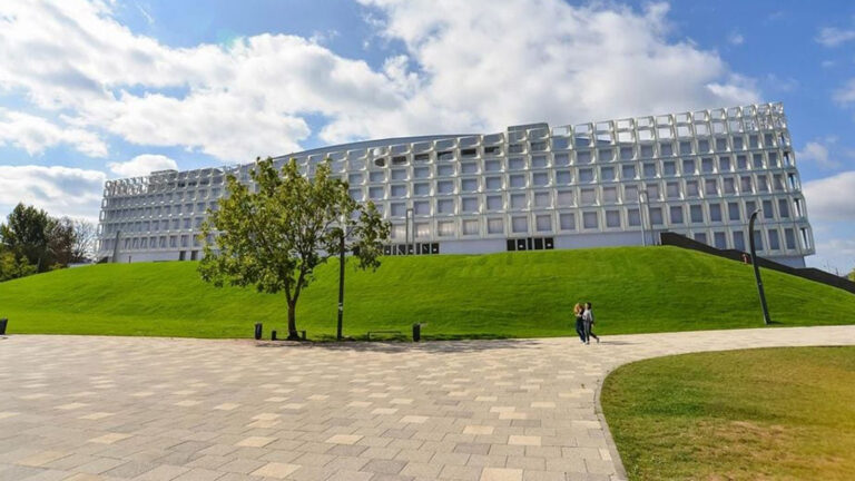 Proiectul unei săli polivalente moderne din București, prezentat într-o zonă verde, sub un cer senin